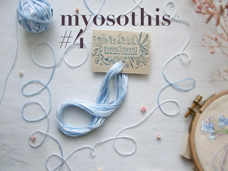 Gros plan sur des fournitures de broderie, notamment des fils bleu clair et blancs, une pelote et une petite carte avec "Dyeing2meetU". Le mot "myosothis" et le numéro "4" sont imprimés sur l'image. Un cercle à broder avec un motif floral est également visible.