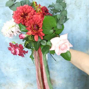May include: A bouquet of pink and red flowers with green leaves and a long, multi-coloured ribbon.