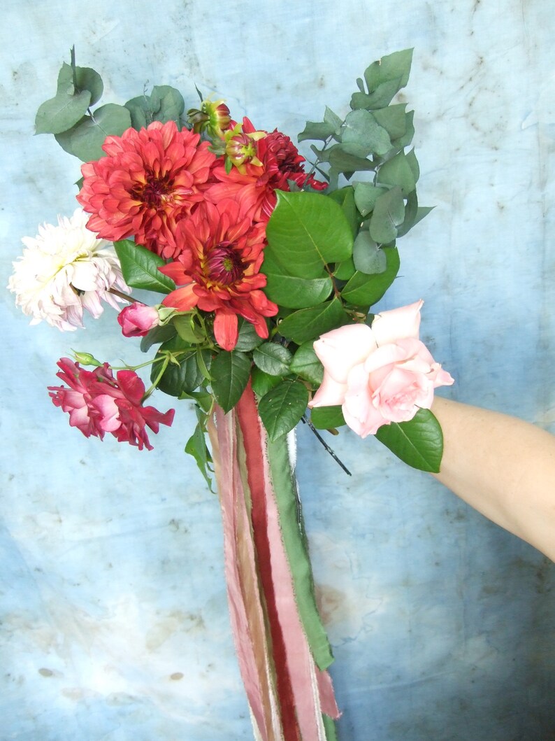 May include: A bouquet of pink and red flowers with green leaves and a long, multi-coloured ribbon.