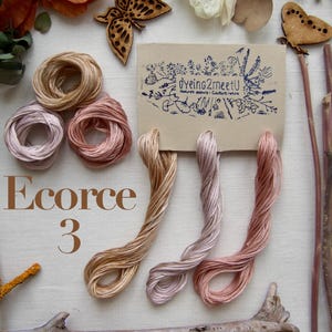 Trois échevettes de fil de coton à broder 6 brins moulinés de 8 mètres chacune, dans des tons gradués de beige, beige gris, beige rose.
Les fils sont présentés sur une carte avec la marque "Dyeing2meetU". Ils sont teints à la main en France. Pour commander il faut sélectionner "3 - Ecorce"