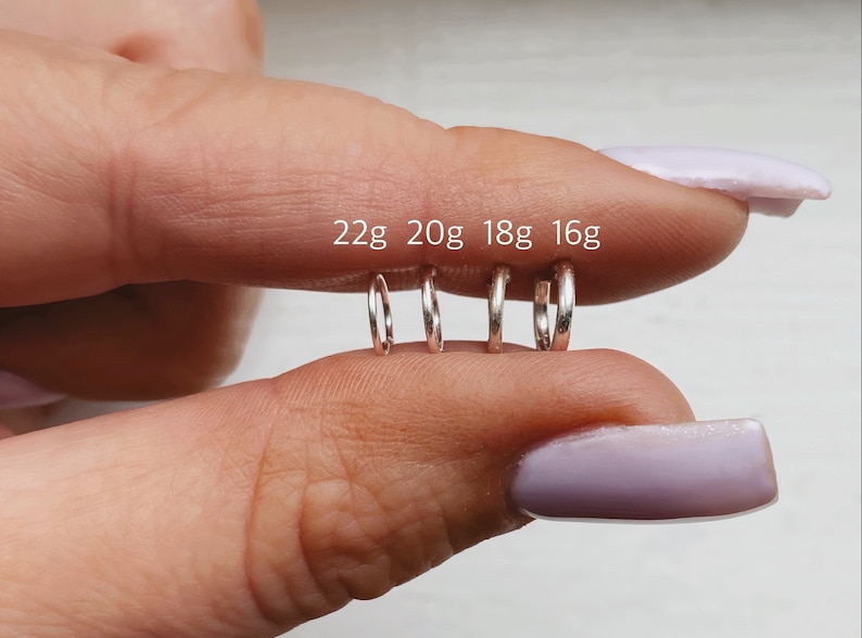 May include: Four silver hoop earrings in different sizes, labelled 22g, 20g, 18g, and 16g. The hoops are held in a person's hand.