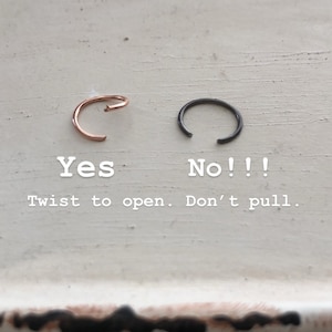 May include: Two nose rings, one gold and one black, on a white surface. The text "Yes" is below the gold ring and "No!!" is below the black ring. The text "Twist to open. Don't pull." is below the rings.