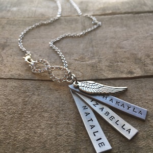 May include: Silver necklace with an infinity symbol charm and four silver tags with the names Makayla, Izabella, Natalie, and a silver angel wing charm.