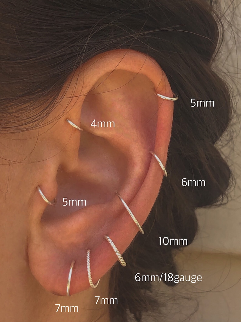 May include: A close-up of a person's ear with multiple silver hoop earrings in various sizes, including 4mm, 5mm, 6mm, 7mm, 10mm, and 6mm/18 gauge.