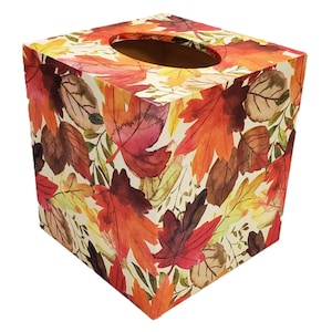 May include: A square tissue box featuring a vibrant autumn leaf design. The box is adorned with watercolor-style leaves in shades of red, orange, yellow, and brown against a cream background. The top has an oval opening for tissue dispensing.