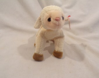 May include: A plush lamb toy with cream-colored fur and brown hooves. The lamb has a pink nose and black eyes. A red tag is attached to its ear. The toy is standing on a white surface.