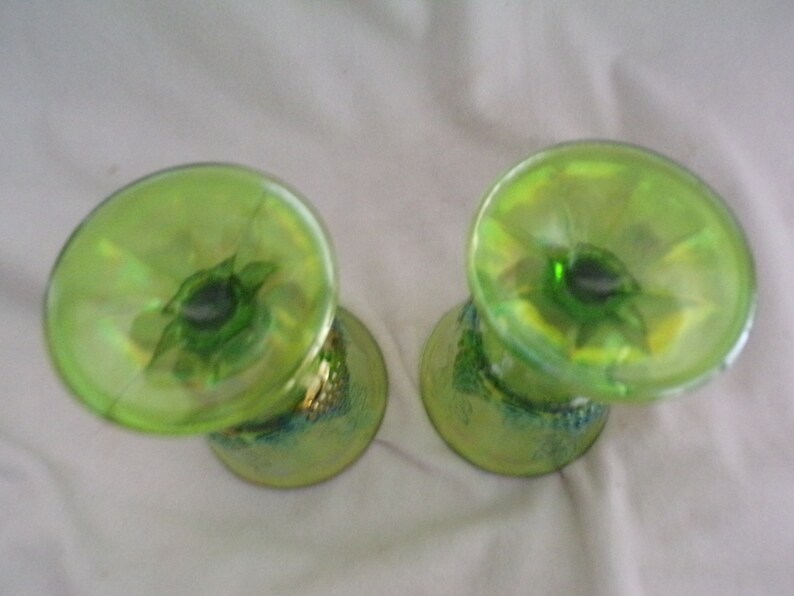 May include: Two green glass cups with a iridescent finish. The cups have a wide base and a narrow top. The base of the cups have a decorative design.