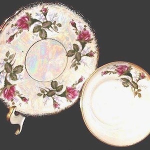 May include: A vintage teacup and saucer set. The white porcelain features a floral design with pink roses and green leaves. The edges are trimmed with gold. The saucer has a scalloped edge and the teacup has a gold handle.