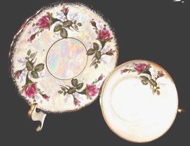 May include: A vintage teacup and saucer set. The white porcelain features a floral design with pink roses and green leaves. The edges are trimmed with gold. The saucer has a scalloped edge and the teacup has a gold handle.