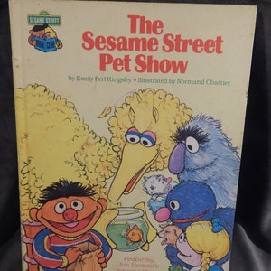 May include: A Sesame Street book cover featuring Big Bird, Elmo, Cookie Monster, and other characters. The title is "The Sesame Street Pet Show" by Emily Perl Kingsley, illustrated by Normand Chartier. The book features Jim Henson's Sesame Street Muppets.