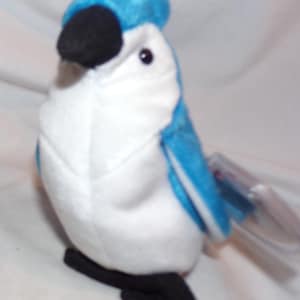 May include: A plush toy bird in shades of blue, white, and black. The bird has a blue head and wings, a white body, and a black beak and feet. It is a soft, stuffed animal, likely for children.