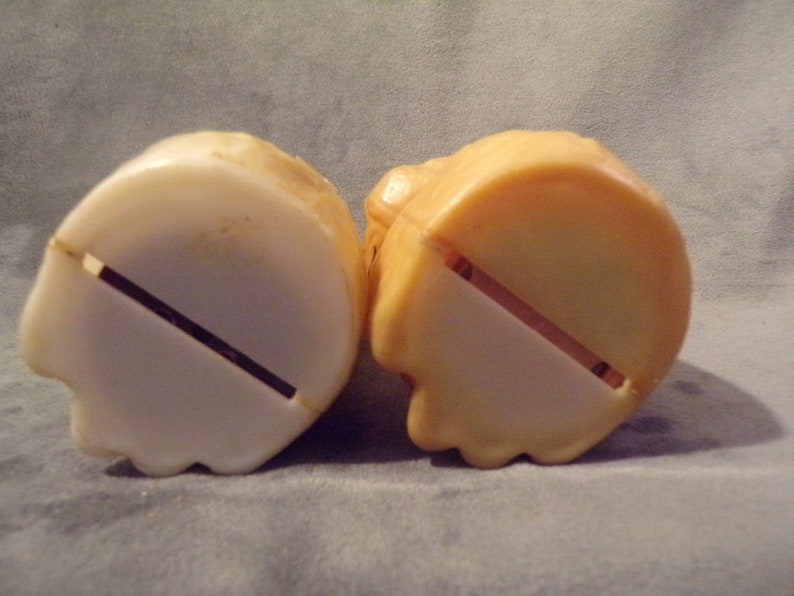 May include: Two plastic piggy banks, one white and one tan, with a slot on the bottom for coins.