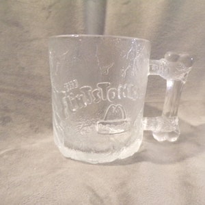 May include: A clear glass mug with a bone-shaped handle. The mug has a frosted finish and the words "The Mister Tortilla" are etched on the front.