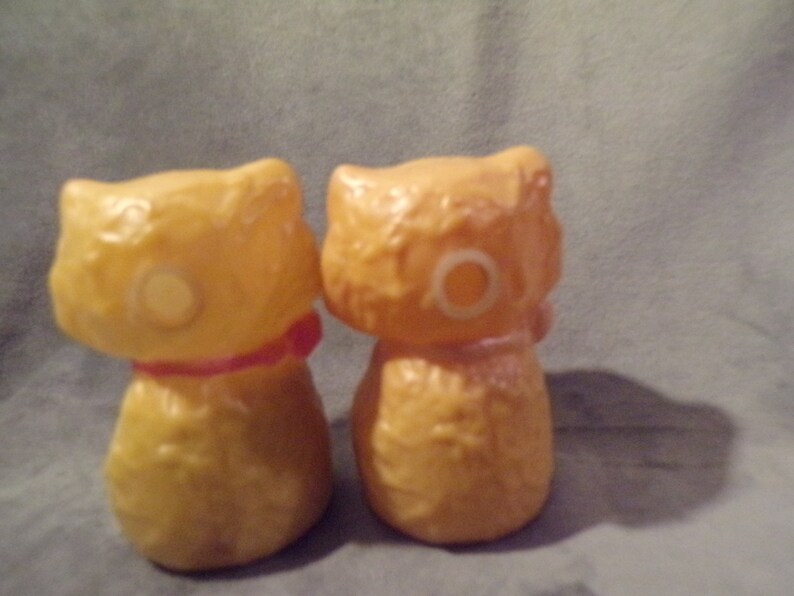 May include: Two yellow ceramic cat figurines with a textured surface. One cat has a red ribbon around its neck.