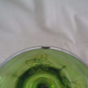 May include: Close-up of the bottom of a green glass goblet with a white rim. The goblet has a decorative design of leaves and vines.