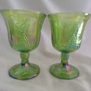 May include: Two green iridescent glass goblets with a grape design. The goblets have a stemmed base and a wide bowl.