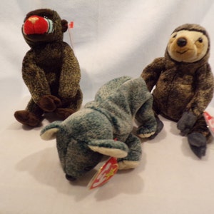 May include: Three plush beanie baby toys: a brown monkey with a red face, a brown sloth, and a green and blue rhino.