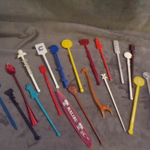 May include: A collection of 19 vintage plastic cocktail stirrers with various designs and colors. The stirrers feature logos and images of brands like Malibu, a giraffe, and a palm tree.