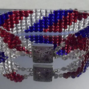 May include: A red, white, and blue beaded bracelet with a silver clasp. The beads are arranged in a pattern that resembles the American flag.