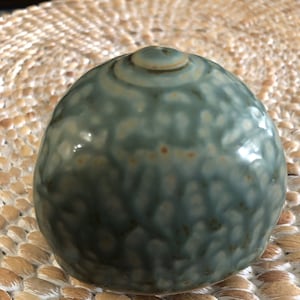 May include: A small, round, ceramic vase with a green glaze and a white speckled pattern. The vase has a smooth, glossy finish.