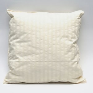 May include: A square, off-white pillow with a subtle striped pattern. The pillow has a soft, slightly wrinkled appearance and is set against a plain white background. The pillow's corners are slightly rounded.
