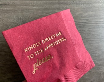 Puede incluir: Una servilleta de color burdeos con letras doradas que dicen "Por favor, dirígeme a los aperitivos."