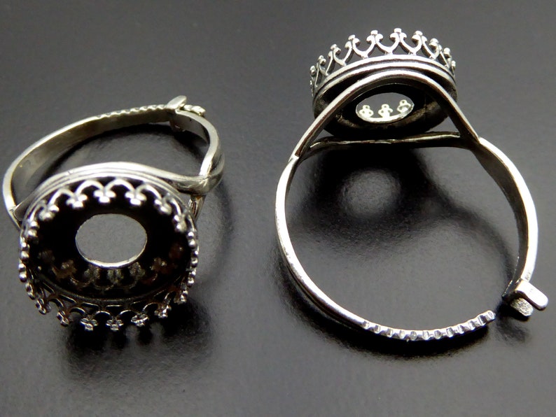 May include: Two silver adjustable ring settings with a round bezel. The bezels have a decorative crown design.