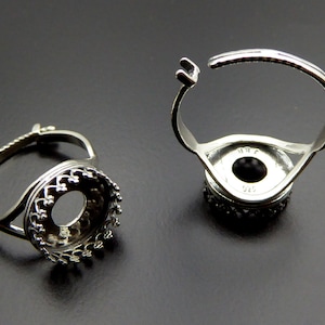 May include: Two silver adjustable ring settings with a round bezel. The bezels have a decorative, scalloped edge. The rings are open on one side and have a spring closure.