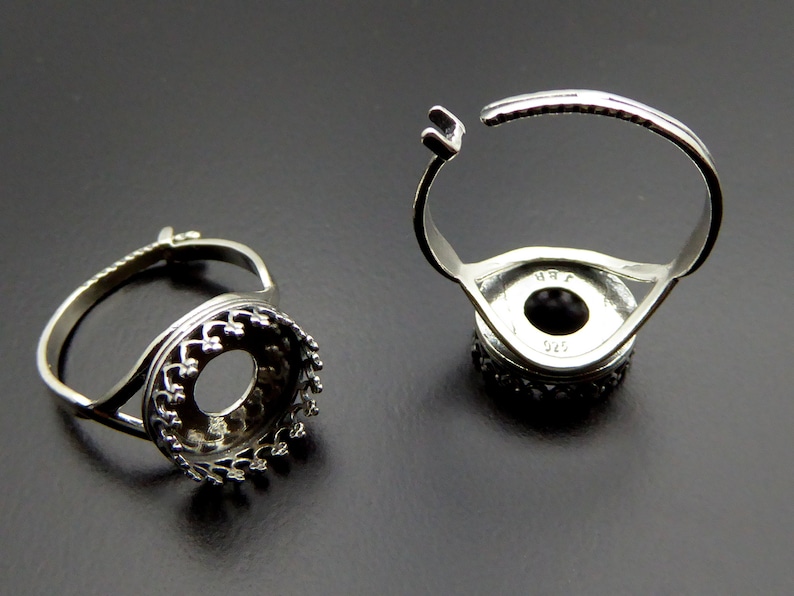 May include: Two silver adjustable ring settings with a round bezel. The bezels have a decorative, scalloped edge. The rings are open on one side and have a spring closure.
