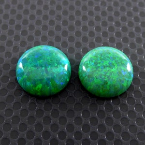 Könnte beinhalten: Zwei runde grüne Opal-Cabochons mit schimmerndem, irisierendem Finish.