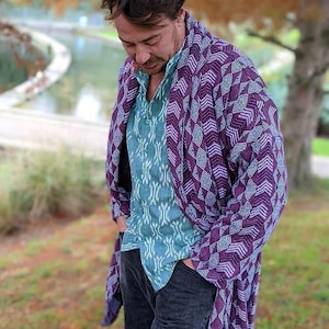 Puede incluir: Un hombre con un chal estampado en morado y azul sobre una camisa estampada en turquesa y pantalones vaqueros azul oscuro.