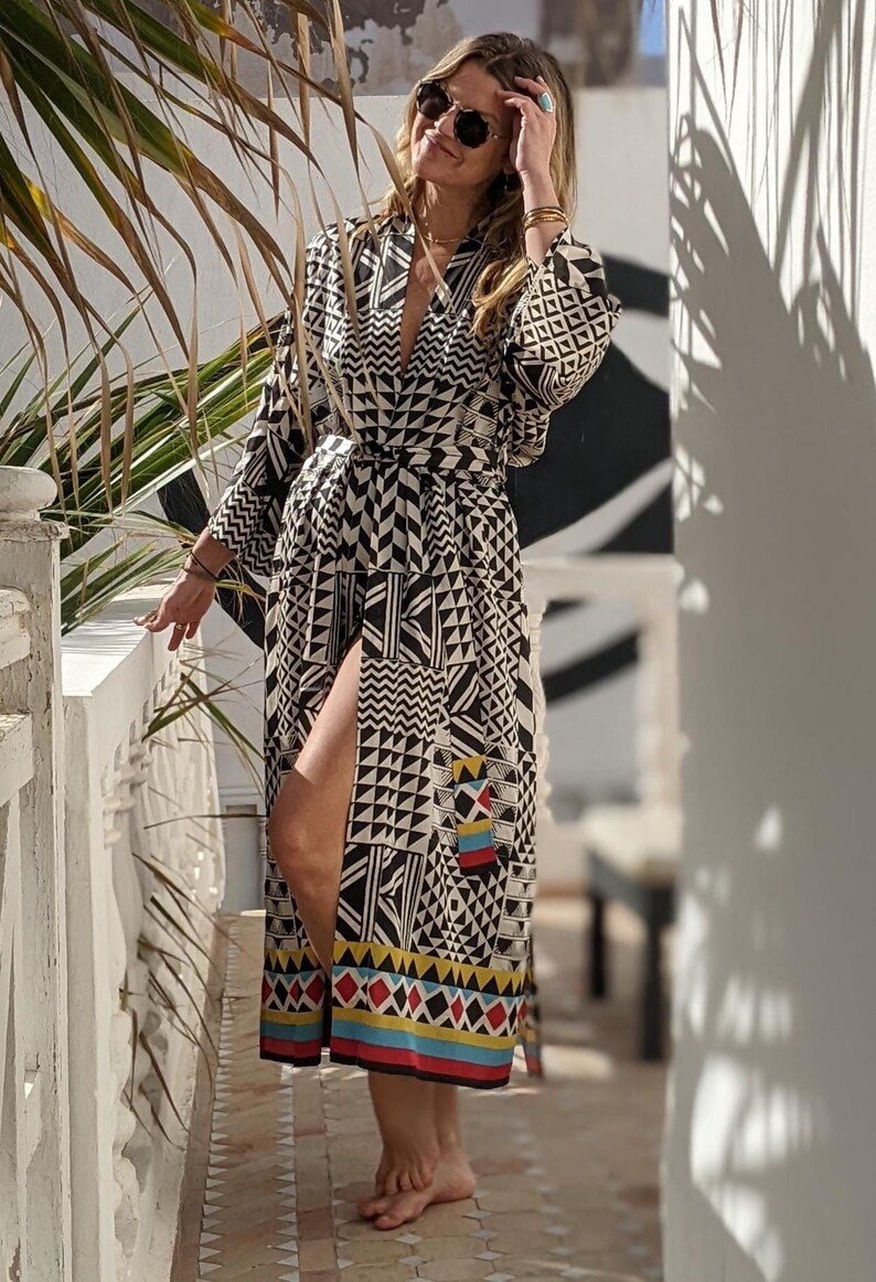 May include: A black and white geometric patterned robe with a long sleeve and a sash tie. The robe has a colorful trim at the bottom.
