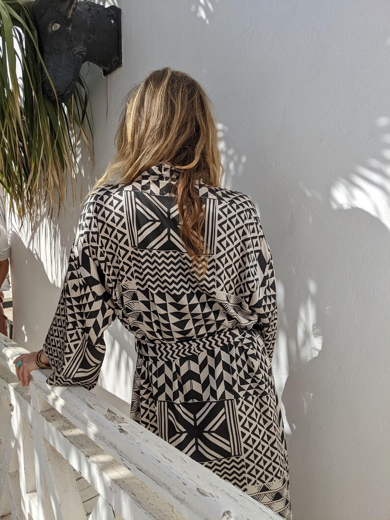May include: A black and white geometric patterned kimono robe with a long sleeve and a sash tie.