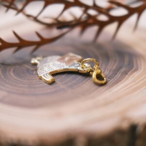 May include: A gold-colored metal charm with a detailed design of a bird with floral accents. The charm has a loop for attaching to a keychain or necklace.