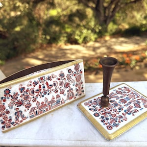 Puede incluir: Un organizador de escritorio blanco y un portalápices con un diseño a juego. El organizador y el portalápices presentan un patrón de arte popular en rojo, azul y dorado. El portalápices es de color marrón oscuro.