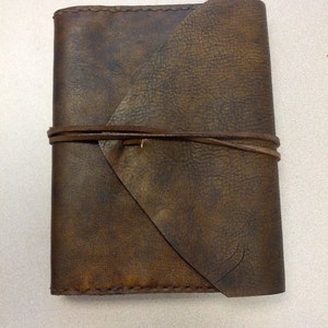 May include: A brown leather journal with a flap closure and a tie closure. The journal has a distressed look and is made of high-quality leather.