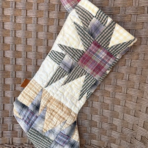 May include: A patchwork Christmas stocking with a star design in shades of green, red, blue, and yellow. The stocking is made of quilted fabric and has a brown leather tag.