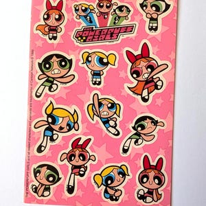 May include: A sheet of Powerpuff Girls stickers on a pink background with white stars. The stickers feature Blossom, Bubbles, and Buttercup in various poses. The Powerpuff Girls logo is also present. Text on the sheet reads: THE POWERPUFF GIRLS and all related characters and elements are trademarks of Cartoon Network © 1999.