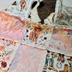 May include: A patchwork quilt with a variety of fabrics, including pink faux fur, floral prints, and a cowhide pattern. The quilt is edged with white pom-poms.