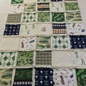 May include: A patchwork quilt featuring golf-themed fabric squares. The quilt showcases various patterns, including golfers, golf courses, argyle, and the text "BORN TO GOLF." Predominantly green, white, and navy blue, it's a cozy, handmade item.