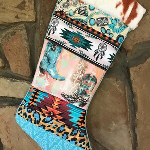 May include: A Christmas stocking with a patchwork design featuring turquoise, brown, and cream patterns. The stocking includes images of cowboy boots, dream catchers, and a cowhide cuff. The overall theme is Western and rustic.