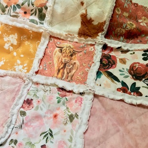 May include: A patchwork quilt with a variety of floral patterns, including pink, red, and yellow flowers. The quilt also features a brown and white cowhide pattern and a square with a brown and white highland cow and calf.