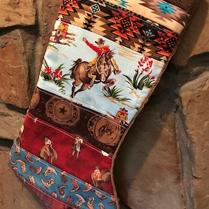 May include: A patchwork Christmas stocking featuring horizontal fabric panels with western themes. Patterns include a cowboy riding a horse, brown leather textures with stars, red fabric with riders, and blue fabric with cowboy boots and the word SADDLE.