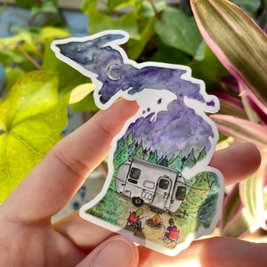 May include: A watercolor illustration of the state of Michigan with a starry night sky, a crescent moon, and a camper van parked in a forest setting. Two people are sitting by a campfire in front of the camper.