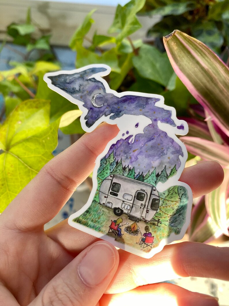 May include: A watercolor illustration of the state of Michigan with a starry night sky, a crescent moon, and a camper van parked in a forest setting. Two people are sitting by a campfire in front of the camper.