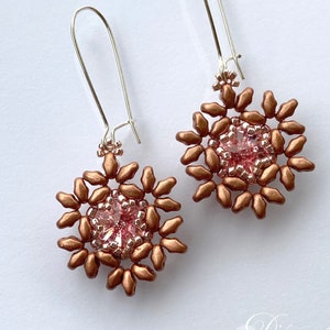 May include: A pair of dangle earrings with a copper-colored beaded flower design and a pink crystal in the center. The earrings have silver hooks.