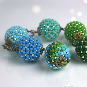 May include: A beaded bracelet featuring spherical beads in shades of blue and green, accented with gold-colored beads. The beads are connected by antique bronze-colored metal links. The bracelet is handmade and has a unique, textured appearance.