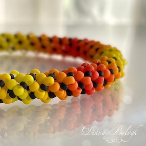 May include: A close-up of a colourful beaded bracelet with a gradient of yellow, orange and red beads. The beads are interspersed with black beads, creating a unique pattern.