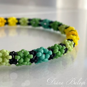 May include: A colourful beaded bracelet with a spiral design. The bracelet features a gradient of yellow, green, and teal beads, with black beads interspersed. The intricate pattern is visible in this handmade piece.