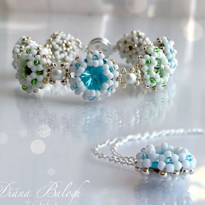 May include: A white and green beaded bracelet with a blue crystal charm and a matching white and blue beaded necklace with a blue crystal charm.